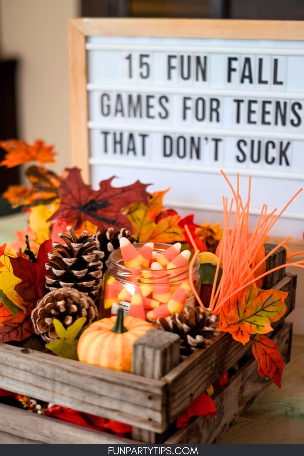 A-wooden-box-filled-with-fall-leaves-pinecones-and-a-jar-of-candy-corn-sitting-beneath-a-sign-that-says-15-Fun-Fall-Games-for-Teens-That-Don’t-Suck.-This-display-creates-a-fun-fall-aesthetic-for-teens.